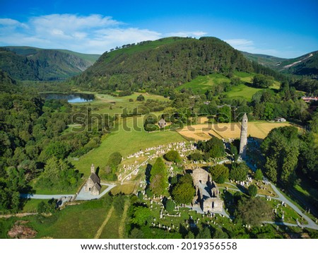 Aerial view of Glendalough monastery settlement and graveyard with surrounding valleys and nature in the background.