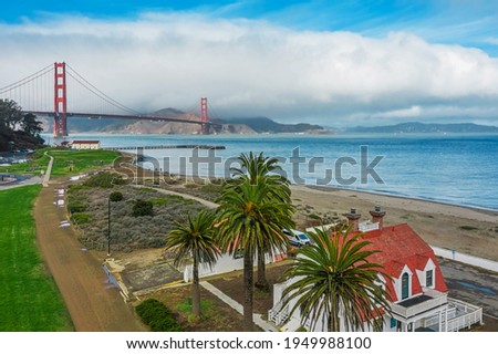 Aerial view of the Golden Gate Bridge from Presidio, against the backdrop of beautiful palm trees in San Francisco, bright sunny weather, palm trees and green grass on the lawn.