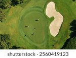 Aerial view of a golf course captured by drone, showcasing golfers on the green with a sand bunker