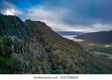 Aerial view of Grampians National Park. A breathtaking aerial view showcasing a dense forest covering rolling hills, with rugged rocky ridges leading toward a serene lake. - Powered by Shutterstock