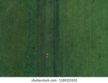 Aerial View Of A Grassy Field With A Woman Laying On Her Back In A Red Dress