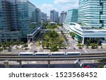 Aerial view of a green open space surrounded by modern office buildings and a metro train traveling on the elevated rails of Wenhu MRT line on a sunny day, in Nankang Software Park, Taipei, Taiwan