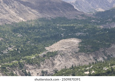 Aerial view of a green valley with scattered houses and tall trees, surrounded by rugged mountains. Lush vegetation contrasts with the rocky terrain, showcasing nature and human settlement. - Powered by Shutterstock