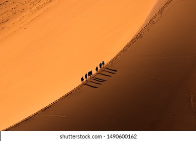 Aerial View Group Of People Walking On The Sand Dune In The Desert And Sun Gradually Create Beautiful Scene.