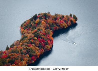 Aerial view of Hachodejima 八丁出島 peninsula blanketed with amazing fall colors and a tour boat cruising on the peaceful water of Lake Chuzenji 中禅寺湖, in Nikko National Park, Tochigi Prefecture, Japan