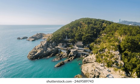 an aerial view of Haedong Yonggungsa Temple in Korea, beautifully situated on a rocky coastline with a clear blue sea, pine trees, and bright sunlight. - Powered by Shutterstock