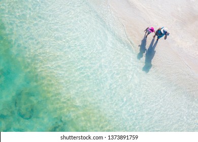 Aerial view. Happy young mum with children holding hand and walking together on tropical shore. Colorful turquoise sea. Peaceful andaman sea at Koh Lipe, Satun, Thailand.