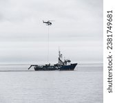 An aerial view of a helicopter lifting supplies from a research vessel in Umnak, Alaska