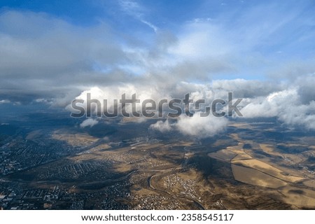 Aerial view from high altitude of distant city covered with puffy cumulus clouds forming before rainstorm. Airplane point of view of cloudy landscape