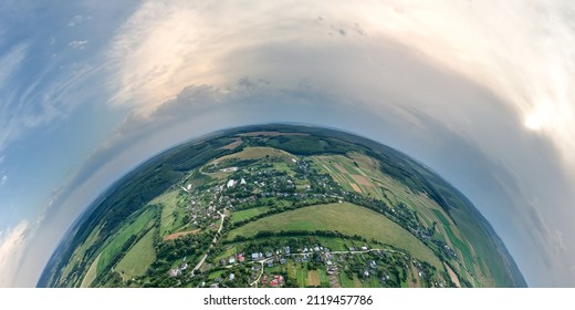 Aerial view from high altitude of little planet earth with small village houses and distant green cultivated agricultural fields with growing crops on bright summer day