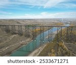 Aerial view of the High Level Bridge spanning over the Oldman River in Lethbridge, Alberta, with a scenic landscape in the background.