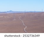 Aerial view of a high-voltage powerline tower in a vast desert, highlighting the contrast of industry and nature.