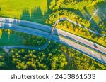 Aerial View of Highway Bridged by a Bicycle Path. Overhead view showcasing the convergence of multiple roadways with vehicles, surrounded by lush greenery, bathed in the warm glow of the setting sun.