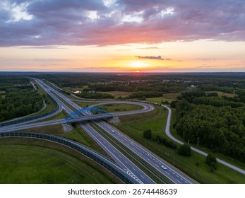 Aerial view of a highway intersection surrounded by lush green fields at sunset. Roads lead into the horizon, showcasing the beauty of nature and infrastructure.