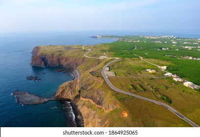 Aerial view of a highway winding along the beautiful coast line of Cimei Island on a sunny day, in Penghu, Taiwan, with a wave-cut platform in the shape of a mini-Taiwan under the rugged seaside cliff