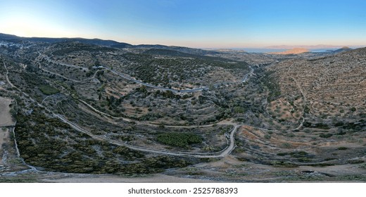 Aerial view of the historic Byzantine Road in Paros, Greece, winding through rugged hills, olive groves, and terraced fields, showcasing the island’s ancient rural landscape at sunset. - Powered by Shutterstock