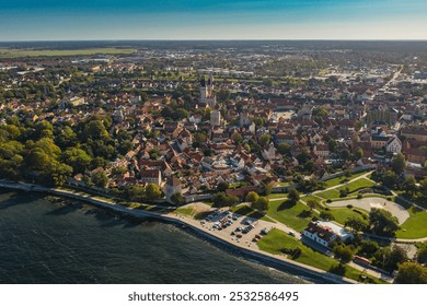 Aerial view of a historic coastal town with medieval architecture, lush greenery, and a winding shoreline. - Powered by Shutterstock