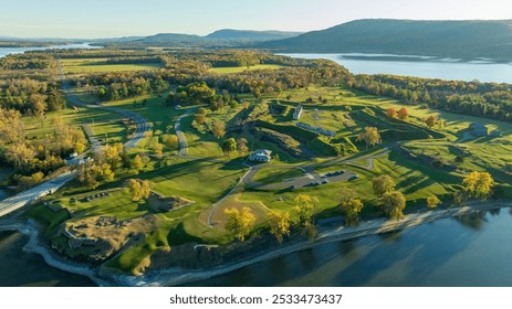 Aerial view of historic ruins along the shoreline, surrounded by lush green fields and autumn foliage, with a lake and distant mountains completing the scenic landscape. - Powered by Shutterstock