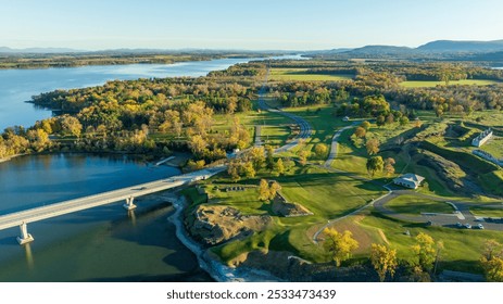 Aerial view of historic ruins along the shoreline, surrounded by lush green fields and autumn foliage, with a lake and distant mountains completing the scenic landscape. - Powered by Shutterstock