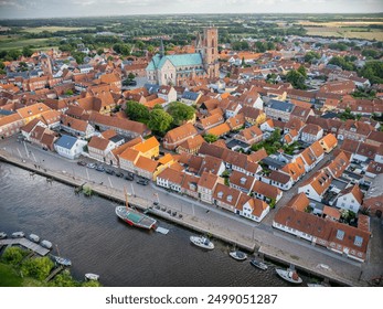 Aerial view of historic town Ribe with majestic Ribe cathedral, red-roofed buildings and boats docked along the riverside, set against lush, green landscape, south-west Jutland, Denmark - Powered by Shutterstock