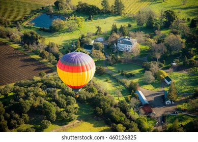 Aerial view of hot air balloon flying over green Napa valley / vineyards / houses on a sunny day