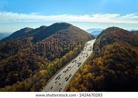 Aerial view of I-40 freeway in North Carolina heading to Asheville through Appalachian mountains in golden fall with moving trucks and cars. Interstate transportation concept