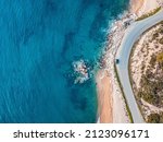 Aerial view of an idyllic sea sandy beach with asphalt winding road and small car driving on. Background for travel and vacation