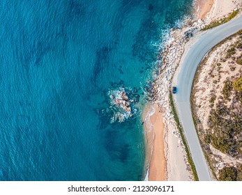 Aerial view of an idyllic sea sandy beach with asphalt winding road and small car driving on. Background for travel and vacation