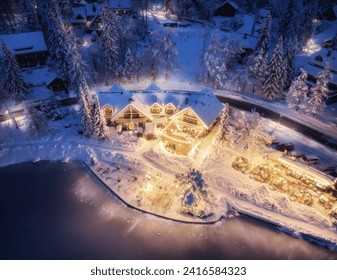 Aerial view of illuminated houses in fairy village in snow, forest, Jasna lake, street lights at winter night. Top view of alpine countryside, snowy pine trees at dusk. Kranjska Gora, Slovenia - Powered by Shutterstock