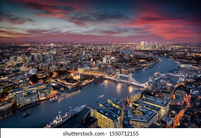 Aerial View Of Illuminated London, UK, During Evening Time Featuring The Tower Bridge, Thames River And The Modern Skyscrapers Of Canary Wharf