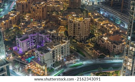 Aerial view to illuminated traditional small houses of old town island night timelapse from above. Dubai downtown with street traffic and trees