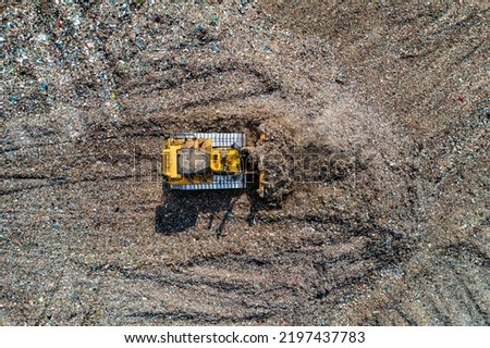 An aerial view of an industrial bulldozer moving household waste and gaebage on a large landfill site