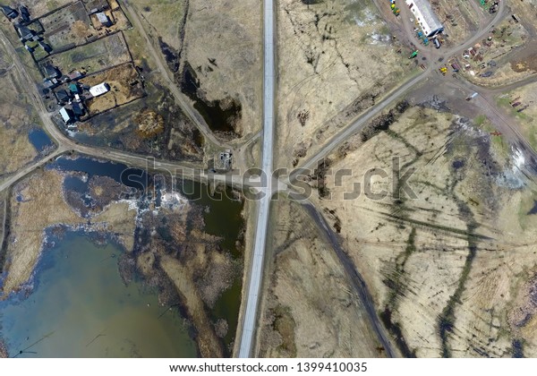 Aerial view\
of the intersection of asphalt and ground roads in the field far\
from the big cities on a clear spring day. Road junction in the\
desert near lake, river, houses and farms.\

