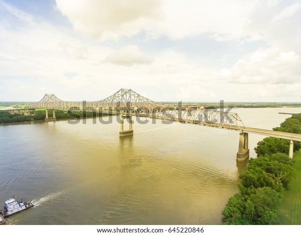 Aerial view of iron cantilever bridge
over the Mississippi river with tugboat pushing an heavy goods
barges in rural Louisiana, America. Cloud blue
sky.