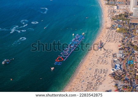 Aerial view of JBR beach in Dubai Marina with inflatable water rides and jet skis in sea