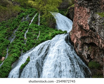 Aerial view of Jermuk Waterfall in Armenia, captured with a DJI Mavic 3 Pro drone. The image highlights the powerful waterfall cascading over rugged cliffs, surrounded by lush green forests. 