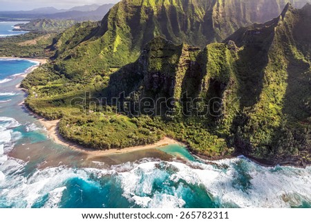 Aerial view of Kee Beach with tall, lush mountains of the Na pali coast and big waves crashing on the reef while on a doors off helicopter tour of Kauai, Hawaii.