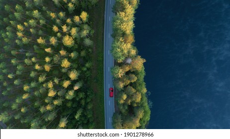 Aerial View Of Lake, Forest And Road At Misty Morning. Red Car Driving Through The Forest At Sunrise. Highway Through Deep Forest.