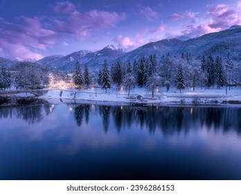 Aerial view of lake, snowy alpine mountains, pine trees in snow, reflection in water, purple sky with clouds at winter night. Nature. Top drone view of beautiful Bohinj lake in Slovenia at sunset - Powered by Shutterstock