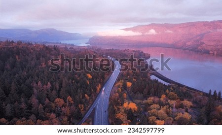 An aerial view of a lake surrounded by autumn trees and hills near a highway in the Dalles, Oregon at sunset