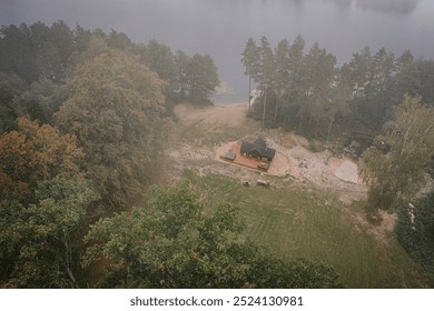 Aerial view of a lakeside cabin with a wooden deck, hot tub, and dock, surrounded by large trees and a small pond in a peaceful natural setting. - Powered by Shutterstock