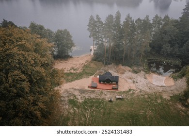 Aerial view of a lakeside cabin with a wooden deck, hot tub, and small dock, surrounded by trees and a pond in a serene natural environment. - Powered by Shutterstock