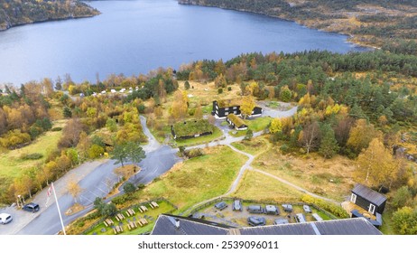 Aerial view of a lakeside campsite surrounded by forested hills. The site includes tents, cabins, and building with green roof. The landscape is dotted with autumn-colored trees, and lake is visible. - Powered by Shutterstock