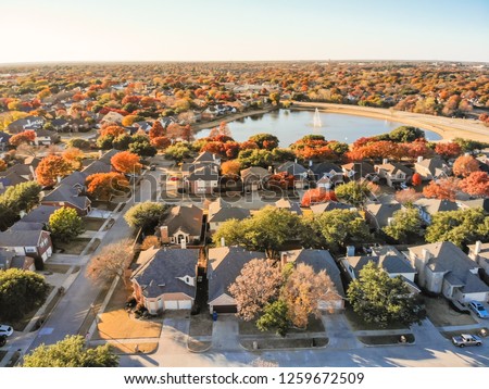 Aerial view lakeside houses neighborhood with colorful autumn leaves. Flyover row of single-family houses with attached garage near lake with water fountain in Flower Mound, Texas, USA