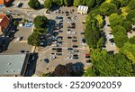 Aerial view of a large parking lot filled with various cars, surrounded by trees and greenery. The layout shows marked parking spaces and a few empty spots.  Ripon, North Yorkshire, UK.