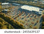 Aerial view of large parking lot in front of rgocery store with many parked colorful cars. Carpark at supercenter shopping mall with lines and markings for vehicle places and directions