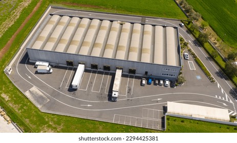 Aerial view of a large shed that is used as a warehouse for loading and unloading parcels. Many trucks are parked around the facility for their work. All within an industrial area.