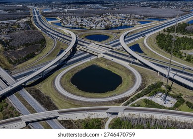 Aerial view of a large stack interchange on Florida's Turnpike. Taken on a sunny day. The camera tilted downward, shows the highway intersection, bodies of water on the landscape.