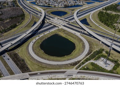 Aerial view of a large stack interchange on Florida's Turnpike. Taken on a sunny day. The camera tilted downward, shows the highway intersection, bodies of water on the landscape.