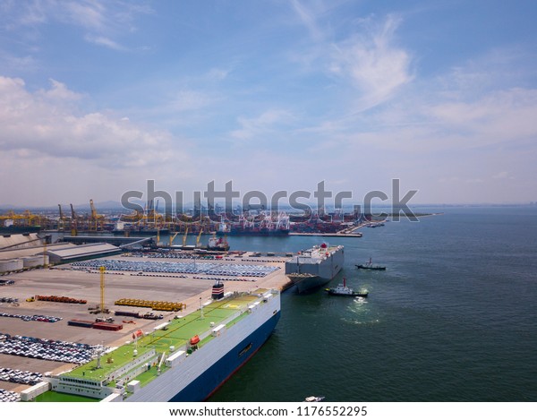 Aerial view of logistics concept floating dry\
dock servicing cargo ship and commercial vehicles, cars and pickup\
trucks waiting to be load on to a roll-on/roll-off car carrier ship\
at Laem Chabang